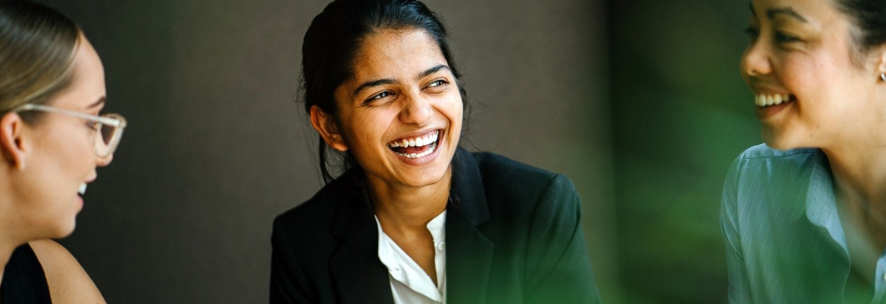 A young Indian Asian woman is having a business meeting with her team in a conference room. Her colleagues are diverse with a Caucasian brunette woman and a Chinese Asian woman